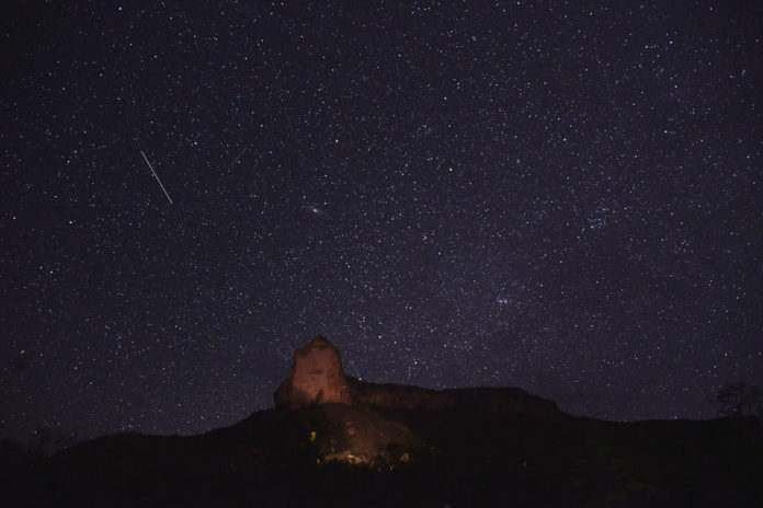 Céu estrelado com um meteoro sobre a silhueta da Serra da Catedral iluminada
