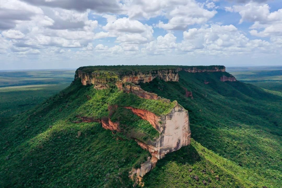 Vista aérea de uma serra de topo plano coberta de cerrado verde, sob céu com nuvens